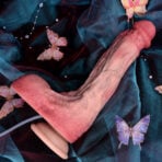 Pink silicone Squirting Dildos Realistic Dildo with a suction base resting on dark blue velvet fabric adorned with pink butterfly decorations.