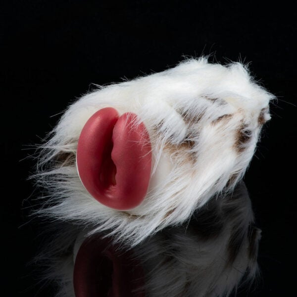 White-furred prosthetic ear with a pink inner ear resting on a black background, likely a makeup/special effects prop.