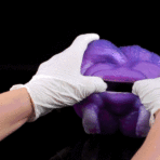 Gloved hands pull apart a sheet of purple slime against a black background
