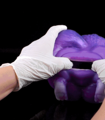 Gloved hands pull apart a sheet of purple slime against a black background