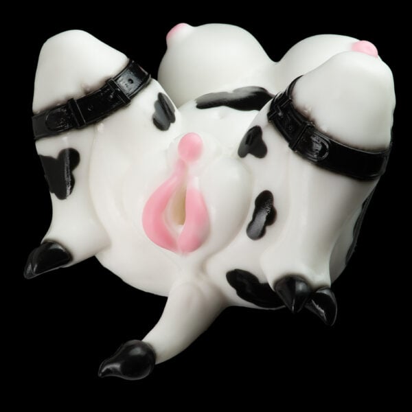 Cow-patterned silicone sex toy with pink udder area and black strap bindings on a black background.