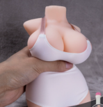 Sex doll torso wearing a white top, being squeezed by a hand at the chest area.